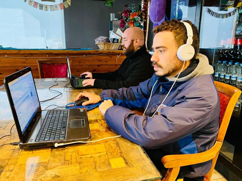 two men sitting at a table with a laptop and headphones at Marco Polo Party Hostel in St. Julianʼs