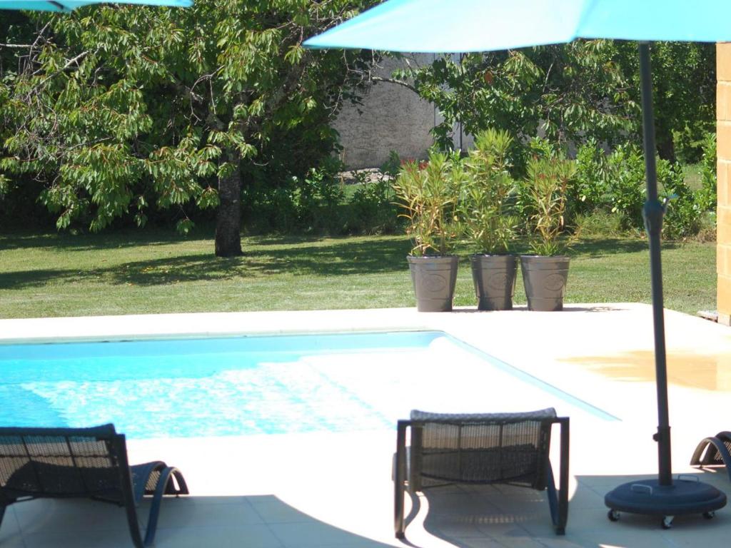 an umbrella and two chairs next to a swimming pool at Gîte Authentique avec Piscine, Cheminée et Étang Privé à Naussannes - Proche Bergerac - FR-1-616-205 in Naussannes