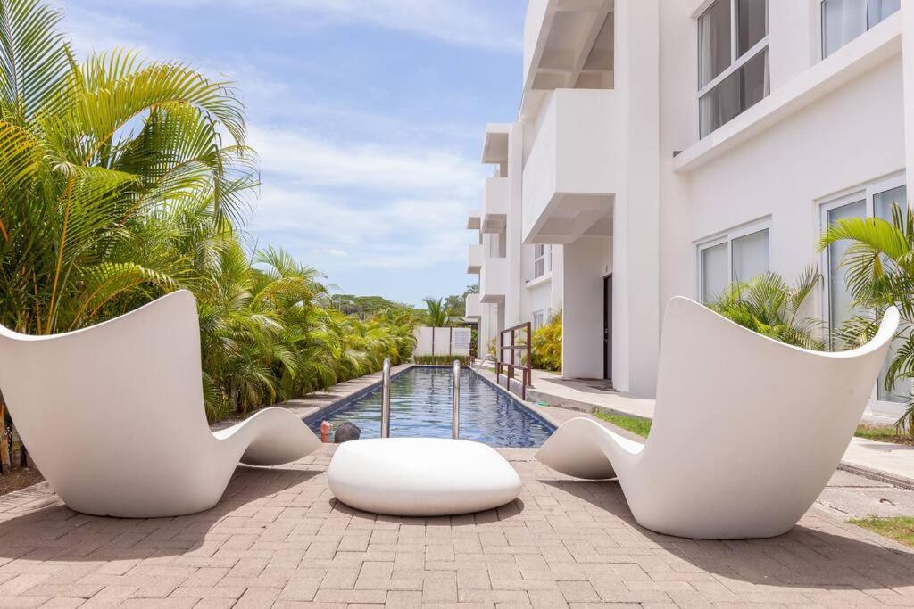a swimming pool with two white chairs next to a building at Bright & Airy new Condo, 5 min walk to Jaco Beach! in Jacó