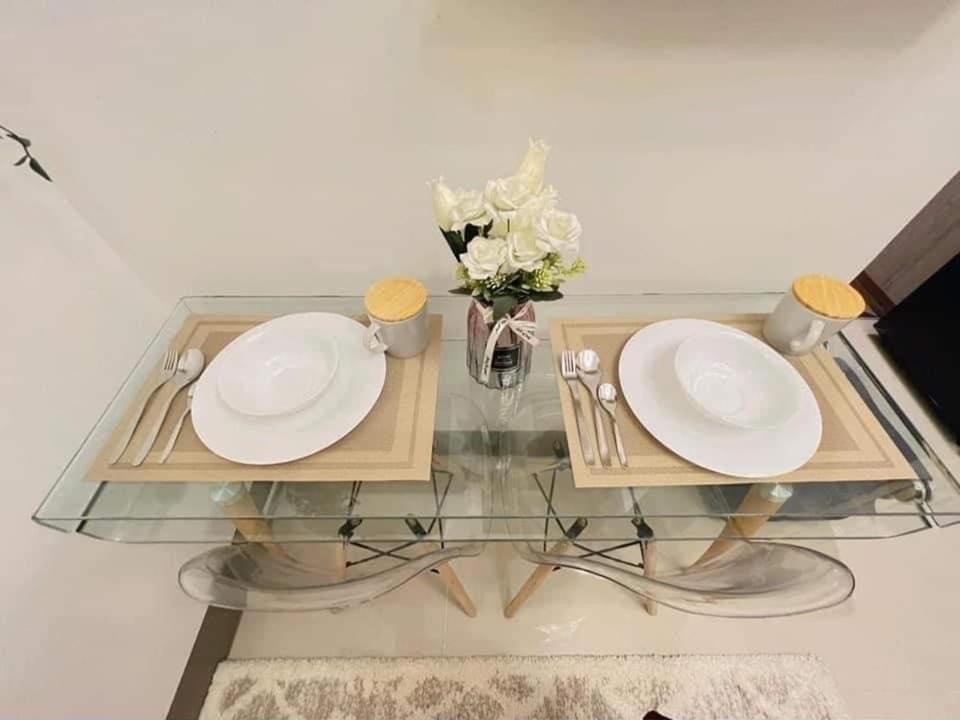 een glazen tafel met twee borden en een vaas met bloemen bij Cozy 1 BR Condo in Fame Residences Mandaluyong City in Manilla