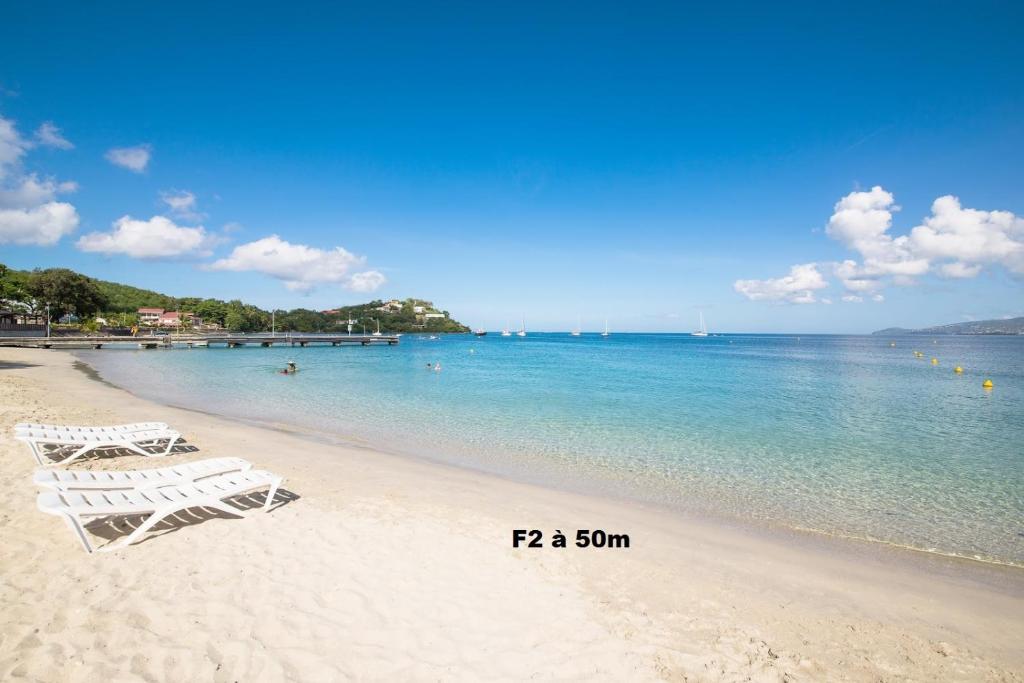 dos sillas blancas en una playa cerca del agua en F2 proche plage Anse Mitan en Les Trois-Îlets