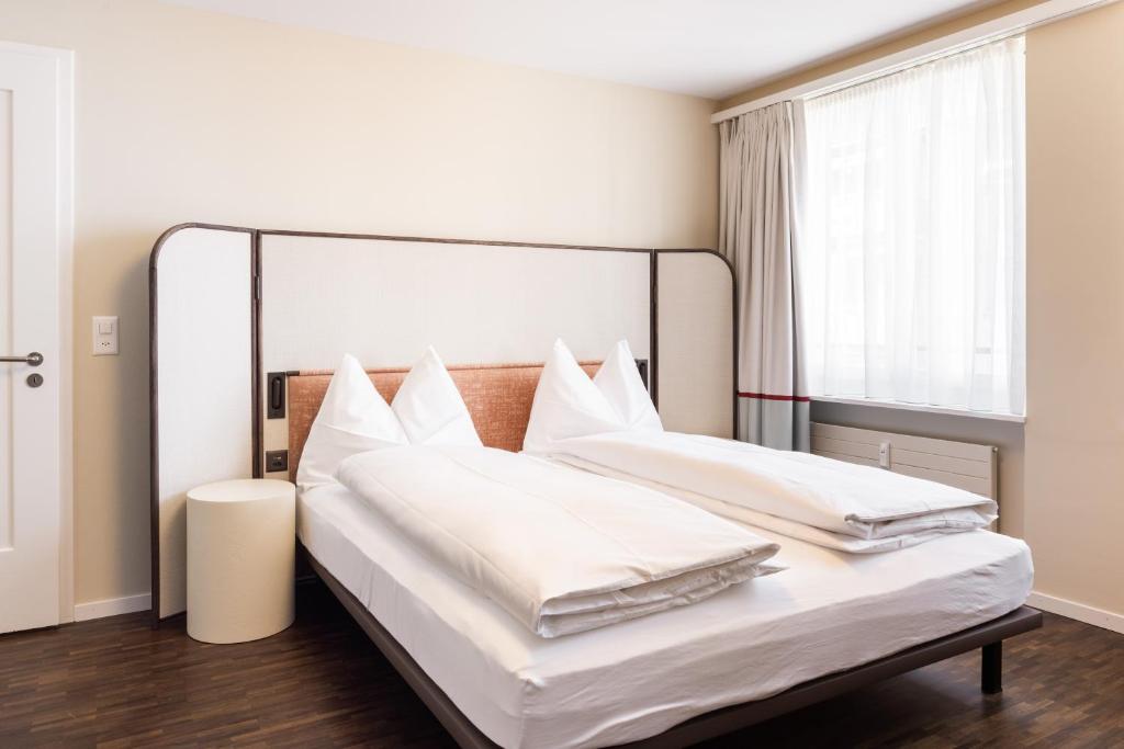una camera con due letti con lenzuola bianche e una finestra di EMA House Serviced Apartments Superior Seefeld a Zurigo