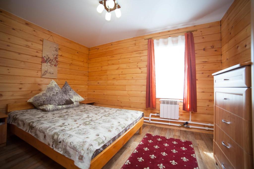 a bedroom with wooden walls and a bed with a window at Guest House Russky Dom in Listvyanka