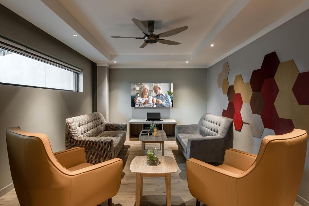 A shared television room arranged with sofas and leather armchairs around coffee tables.