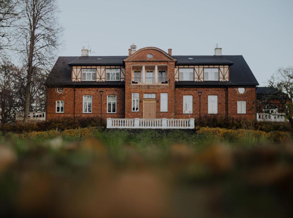 een groot rood bakstenen huis met een zwart dak bij Piena muiža - Berghof Hotel & SPA in Sieksāte