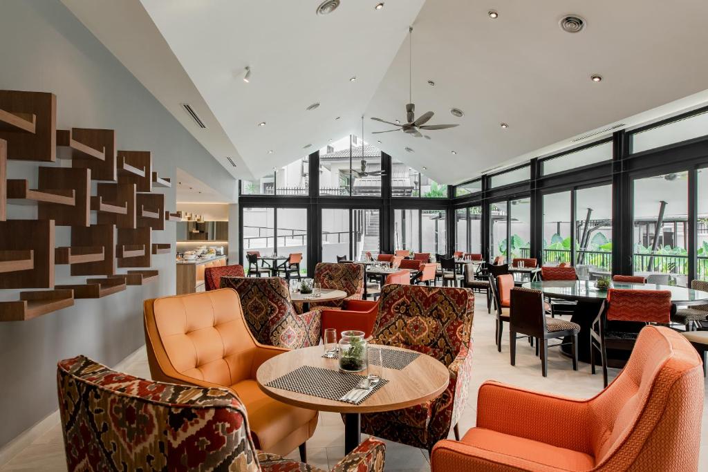 A bright restaurant lounge with floor-to-ceiling windows, patterned armchairs and small dining tables.