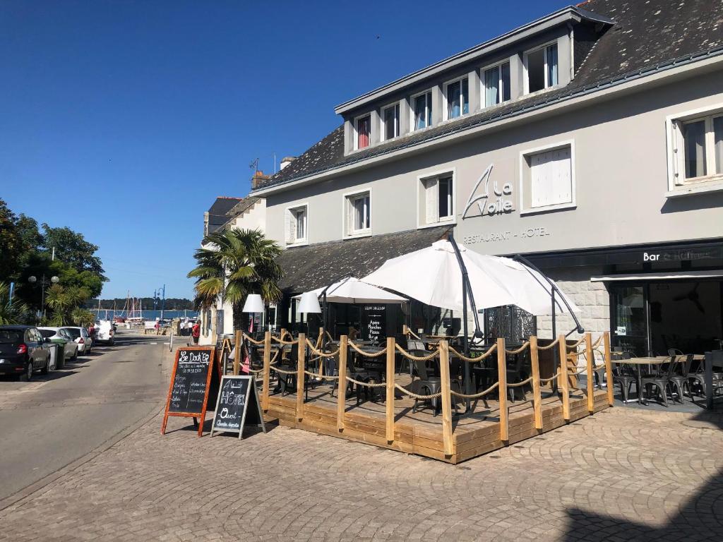 ein Restaurant mit Tischen und Sonnenschirmen vor einem Gebäude in der Unterkunft Hôtel Restaurant La Voile - Le Dock'er in Locmariaquer