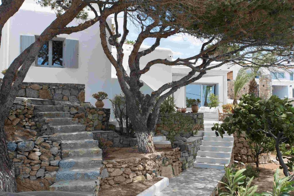 a house with a stone wall and stairs with trees at Mykonos Serendipity Villas in Platis Yialos Mykonos