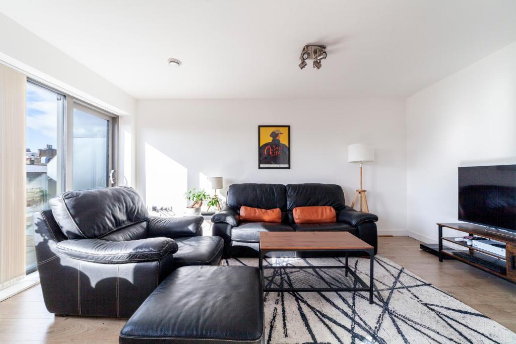 a living room with a black leather couch and a television at Contemporary Top floor flat in Kentish Town in London