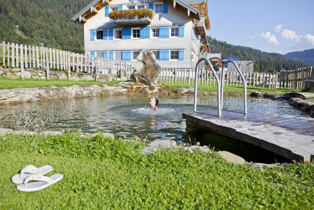 a person swimming in a pond in front of a house at Gasthof Schwabenhof in Balderschwang