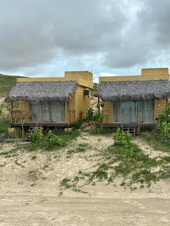 two houses with thatched roofs sitting on a dirt road at Bangalô Encantador Praia da Baleia in Itapipoca