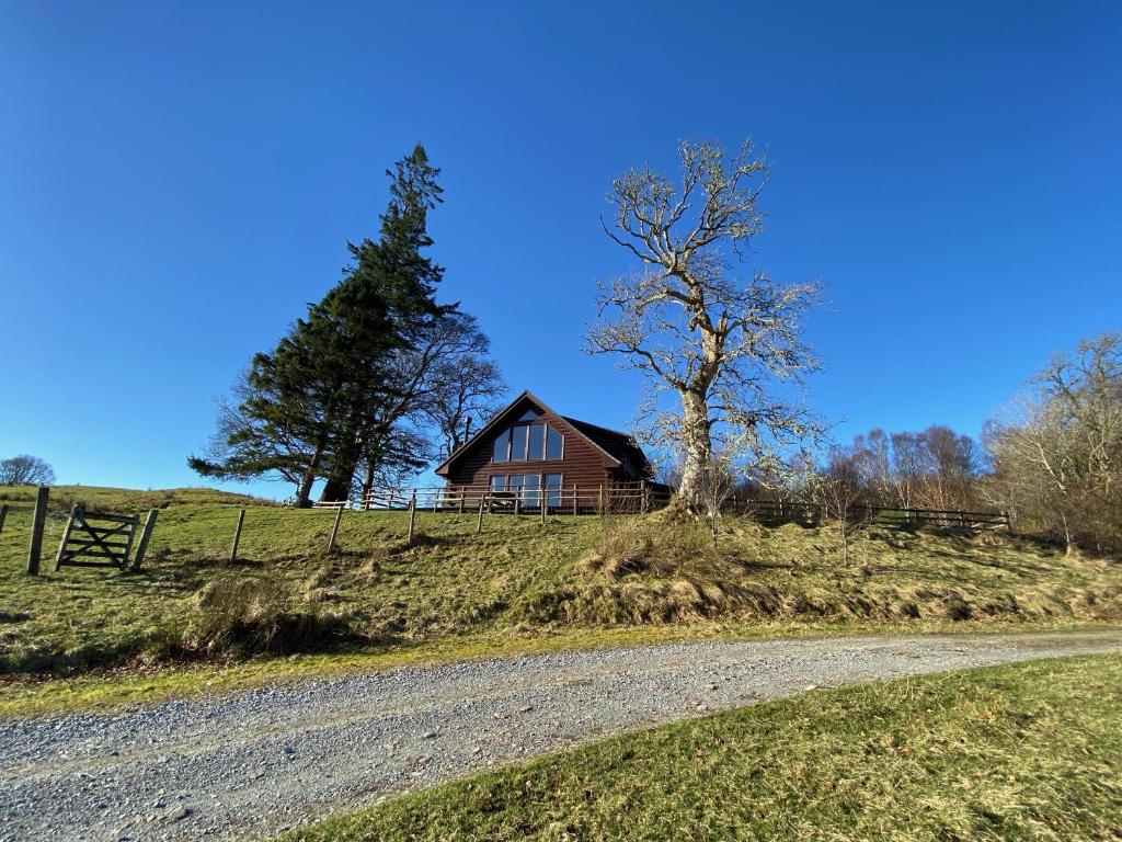 a barn on a hill with a tree and a road at Great Glen Holidays - Lone Pine Lodge in Torlundy