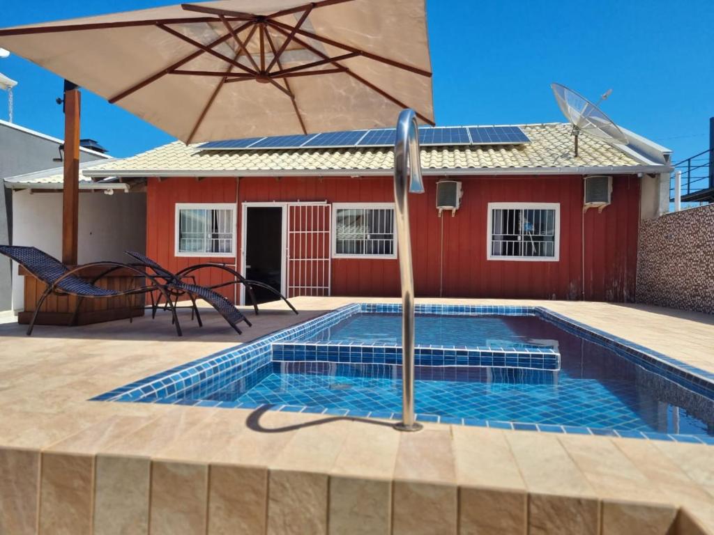 - une piscine avec un parasol et une maison dans l'établissement Casa Marfim - Piscina - Mariscal, à Canto Grande