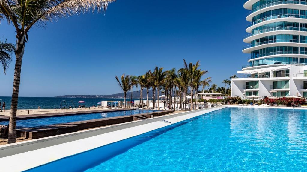 una piscina con palmeras y un edificio en Brand New Condo Aria Ocean 501 by Kivoya en Nuevo Vallarta 