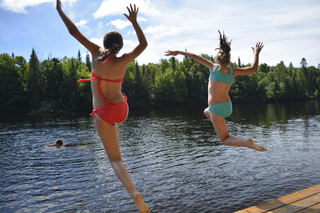 Zwei Mädchen, die an einem See ins Wasser springen in der Unterkunft Chalet bois rond aux paysages uniques avec Spa ! in Lac-aux-Sables