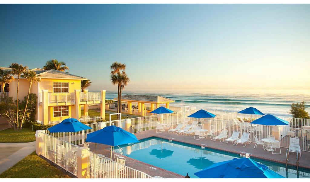 uma piscina com guarda-sóis e cadeiras azuis e o oceano em Gulfstream Manor em Delray Beach