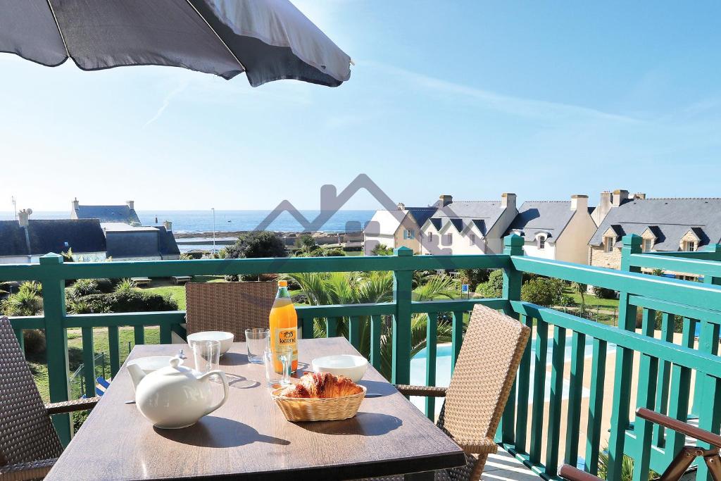 una mesa con un plato de comida y una sombrilla en el balcón en LocaLise au Guilvinec - A28 - Belle vue sur la mer, la piscine et le jardin - - Tout à pied, plages, port, centre, commerces, marché - Wifi inclus - Linge de lit inclus, en Le Guilvinec