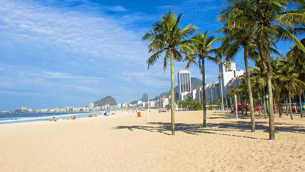 a beach with palm trees and the ocean and buildings at Apartamento Praia Leme Star in Rio de Janeiro