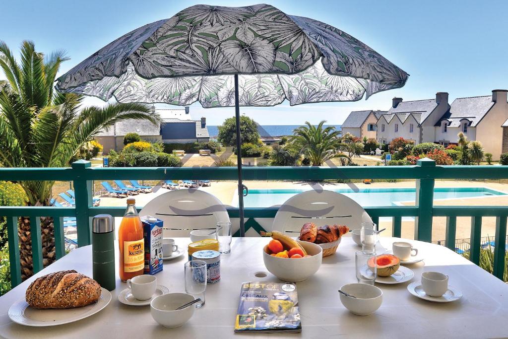 una mesa con comida en un balcón con sombrilla en LocaLise au Guilvinec - A16 - Vue sur la mer, la piscine et le jardin - Tout à pied, plages, port, centre, commerces, marché - Wifi inclus - Animaux bienvenus - Linge de lit inclus, en Le Guilvinec