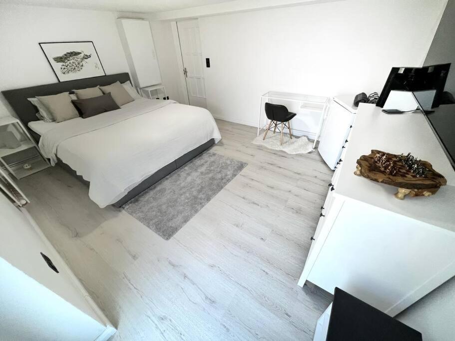 a white bedroom with a bed and a desk with a chair at 2 Zimmer mit gemütlichen Kingsizebett und 58'TV in Hannover