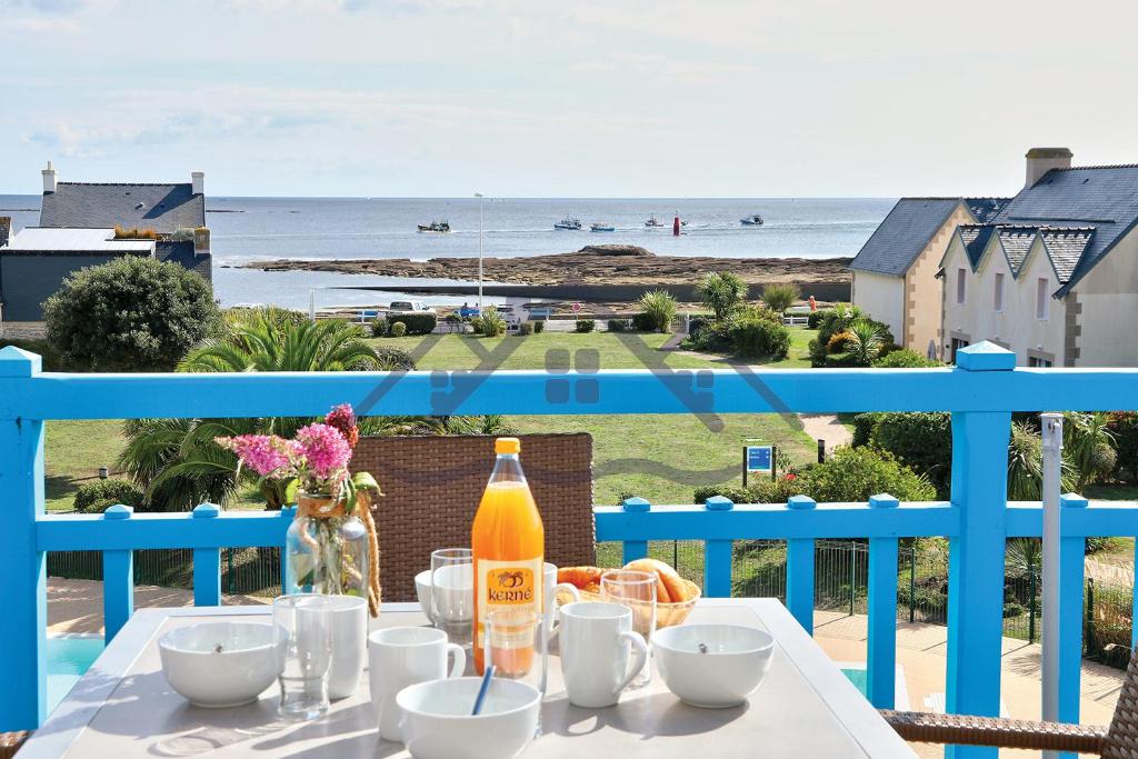 una mesa con una botella de zumo en un balcón con vistas a la playa en LocaLise au Guilvinec - A22 - Belle vue sur la mer, la piscine et le jardin - Tout à pied, plages, port, centre, commerces, marché - Wifi inclus - Animaux bienvenus - Linge de lit inclus, en Le Guilvinec