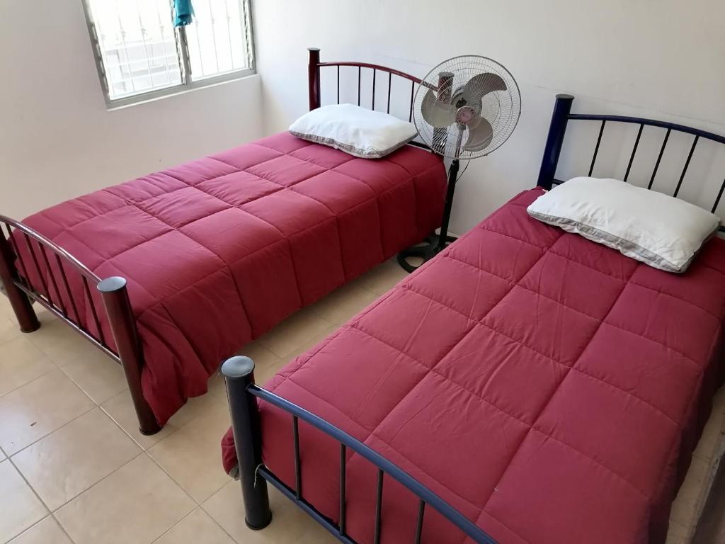 2 bedden met een rode deken en een ventilator bij Casa D vacaciones/negocios/WiFi/CableTV/2Estaciona in Tuxtla Gutiérrez