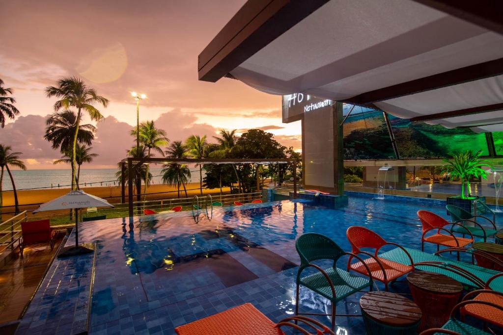 uma piscina com cadeiras e vista para o oceano em Netuanah Praia Hotel em João Pessoa