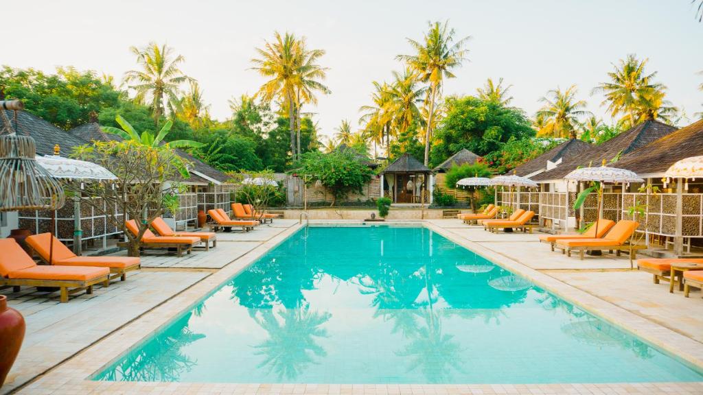 a pool at a resort with orange chairs and palm trees at Les Villas Ottalia Gili Meno in Gili Meno