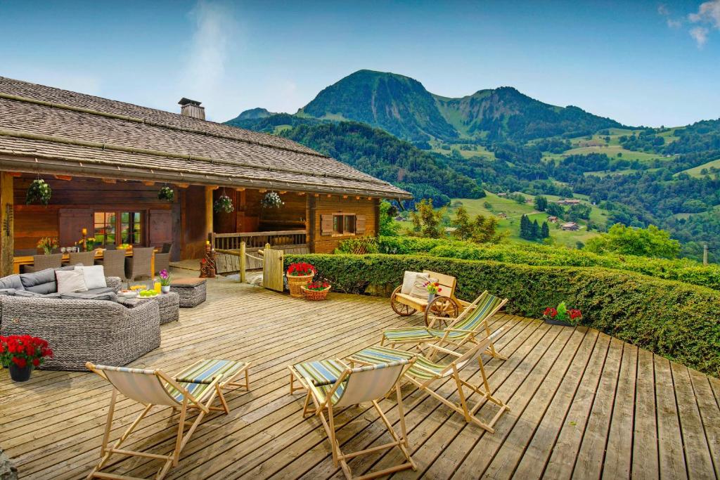 a wooden deck with chairs and a house with mountains at Chalet OVO La Vieille Ferme - OVO Network in Manigod