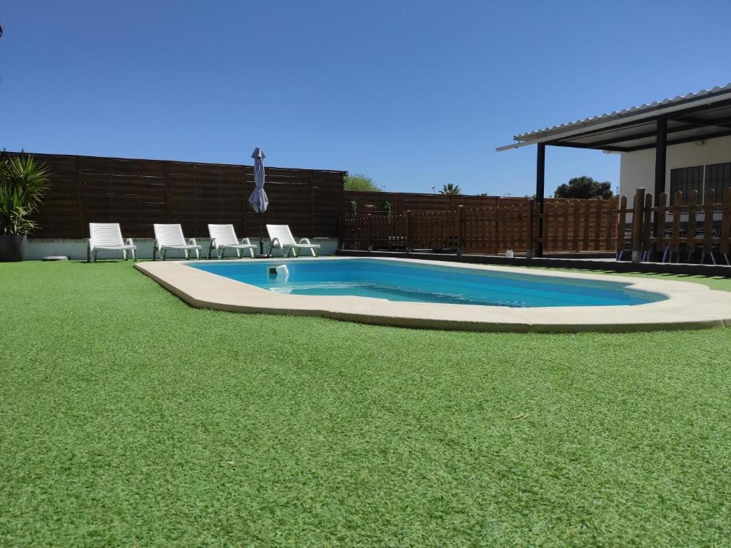 uma piscina num quintal com cadeiras e relva em Chalet en el Aljarafe a 15 min de Sevilla em Sevilha