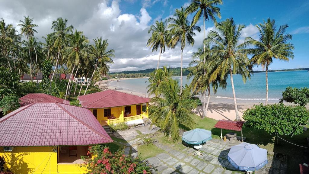 an aerial view of a beach with a yellow house and palm trees at Harus Damai Inn in Lagudri