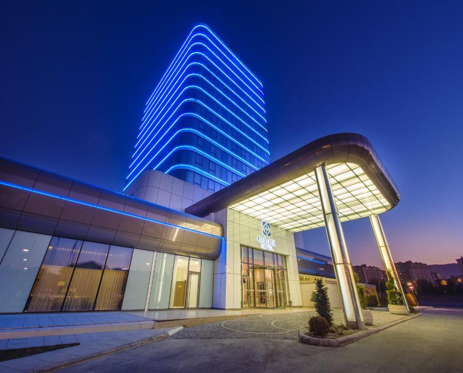 duży budynek z niebieską oświetloną wieżą w obiekcie Ommer Hotel Kayseri w mieście Balqash