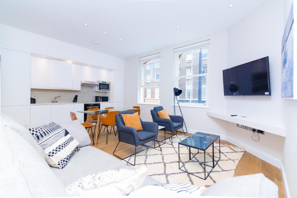 a living room with a white couch and chairs at Whitfield Street Apartments in London
