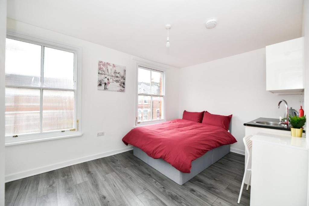 a white bedroom with a red bed and two windows at Waylen Street Suites in Reading