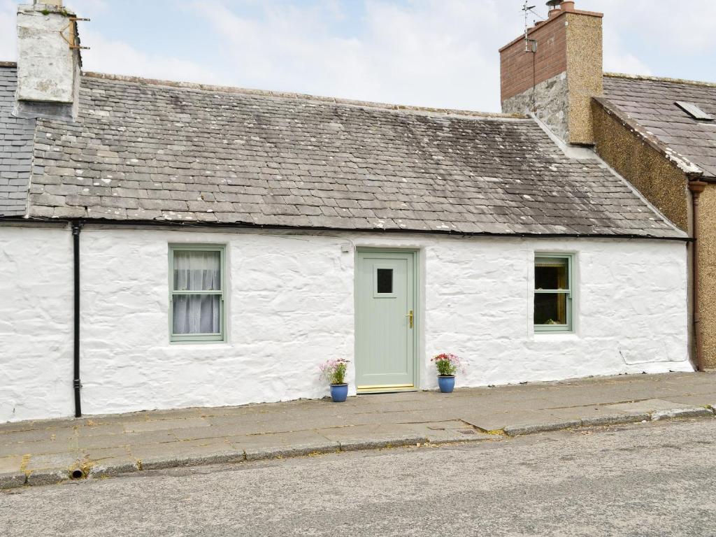 a white cottage with a green door on a street at River Cottage in Bladnoch