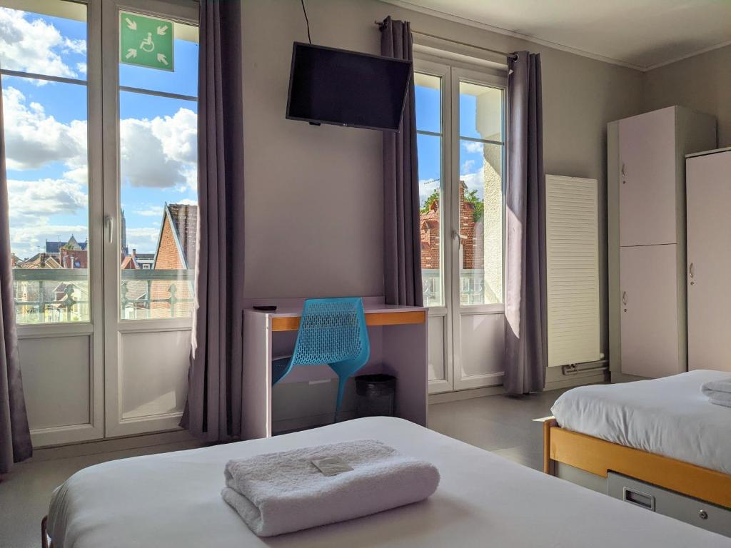 ペロンヌにあるAuberge des Rempartsのベッド2台、デスク、窓が備わるホテルルームです。