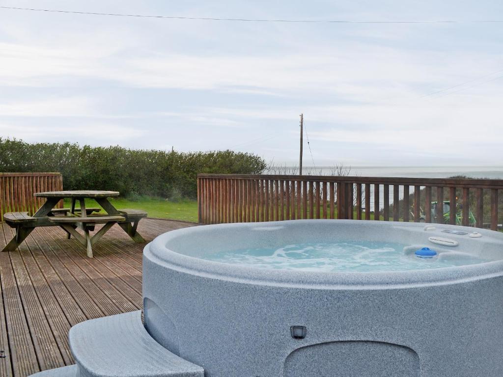a hot tub on a deck with a picnic table at Colman Bach in Llangwnadl