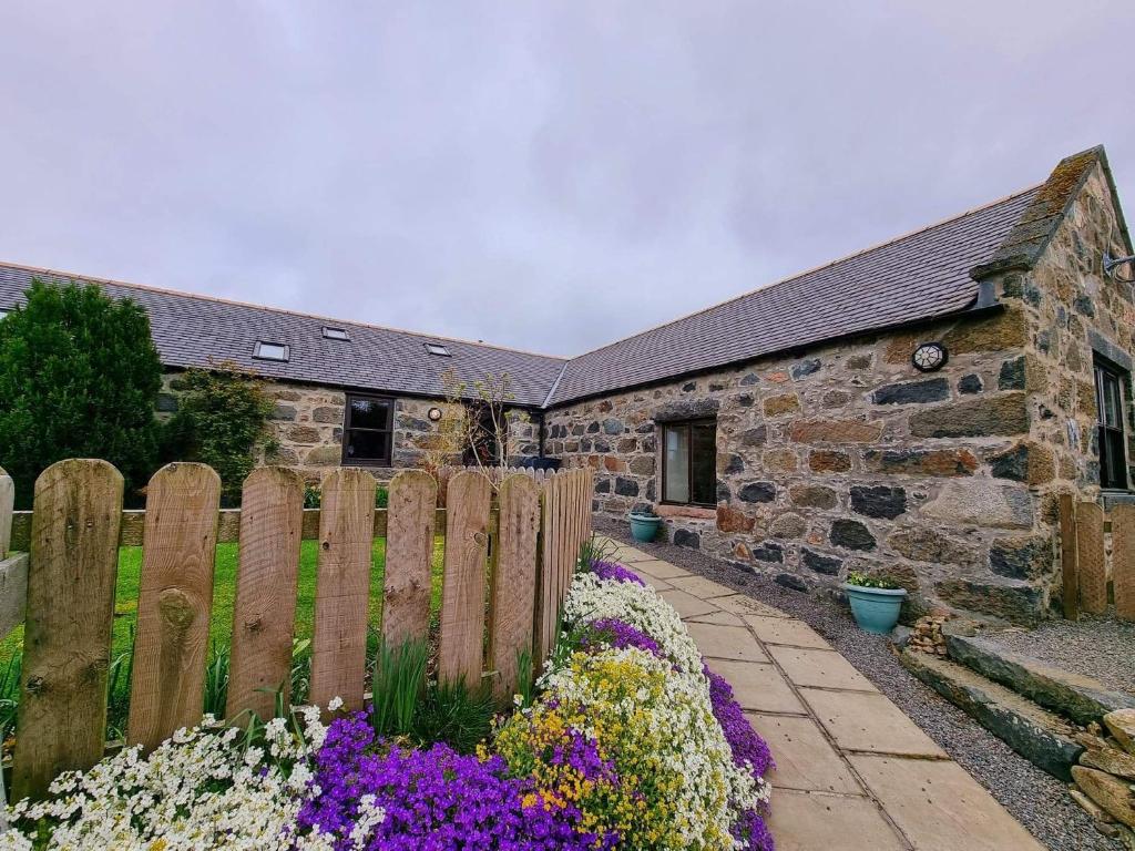 a stone house with a wooden fence and flowers at Barclay’s But n Ben in Alford