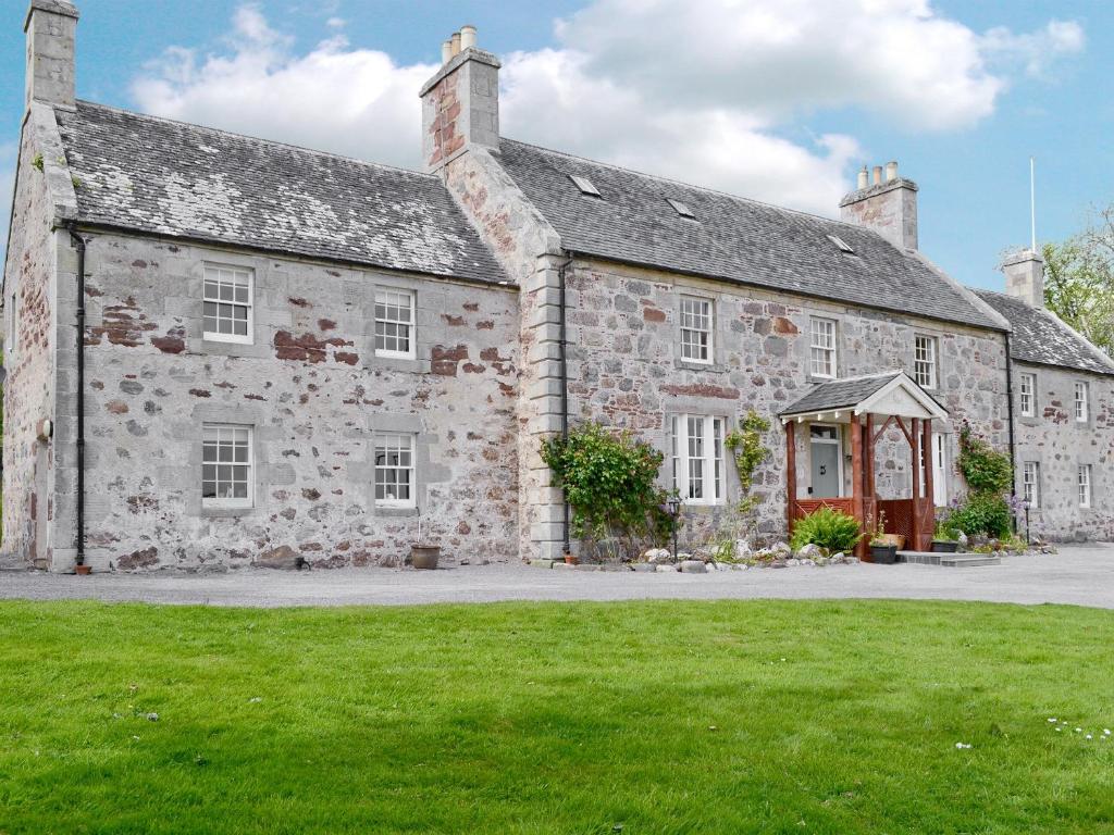 un antiguo edificio de piedra con un césped verde delante de él en Drummuie House en Golspie