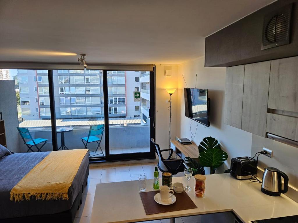 a bedroom with a bed and a kitchen with a view of a balcony at Apartamentos Bauerle Curitiba in Temuco