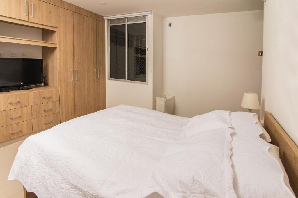 Schlafzimmer mit einem weißen Bett und einem TV in der Unterkunft Apartamento acogedor in Montería