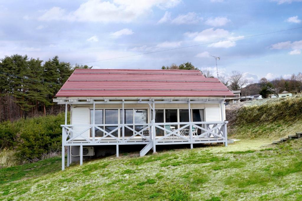 a small white house with a red roof on a hill at ヒュッテ・ボーデン in Komoro