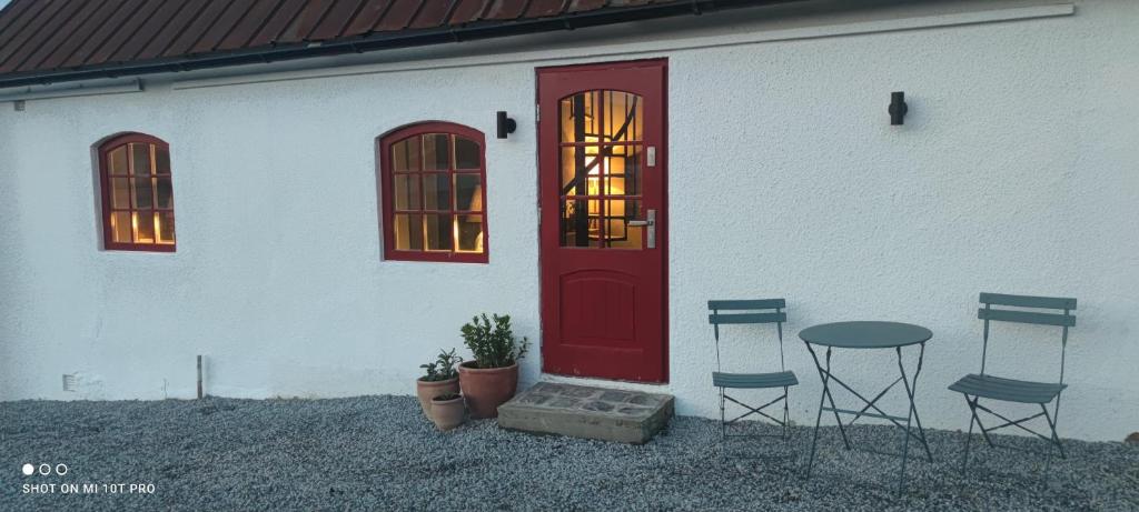 - un bâtiment blanc avec une porte rouge, 2 chaises et une table dans l'établissement Smedjan Mat & Logi, à Östra Ingelstad