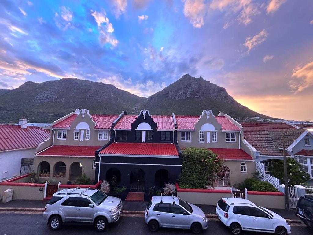 a building with cars parked in a parking lot with a mountain in the background at ‘The Black Pearl’ - Surfers Corner, Muizenburg in Cape Town