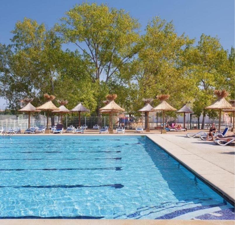 a swimming pool at a resort with chairs and umbrellas at Bungalow dans une résidence en plein air a l'Elysée vagues océanes "capfun" in Le Grau-du-Roi
