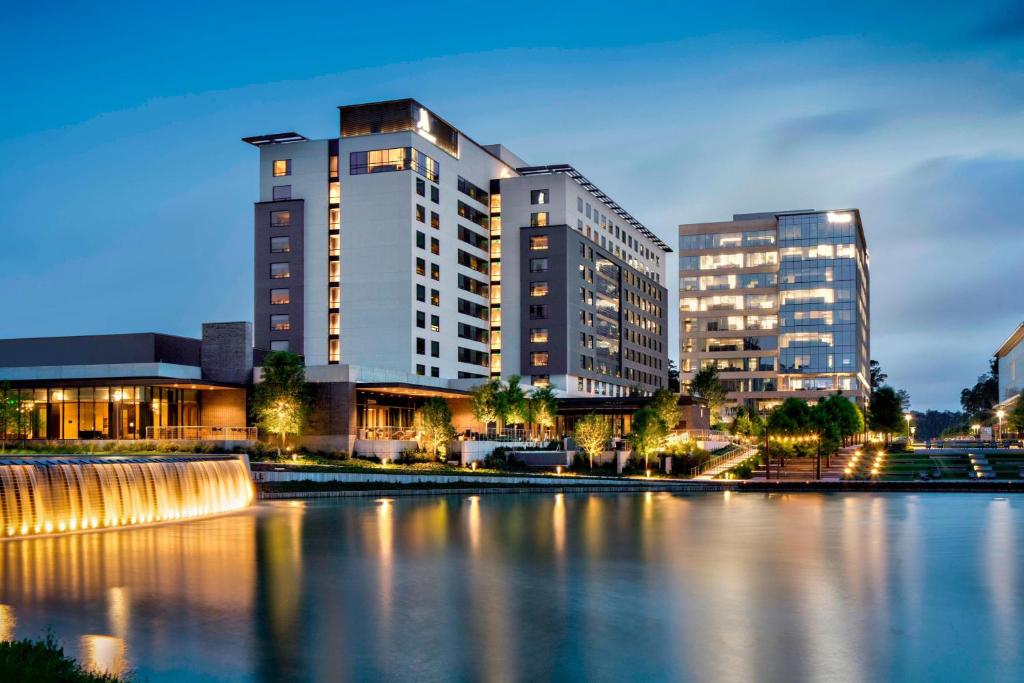 a building next to a body of water with buildings at Houston CityPlace Marriott at Springwoods Village in The Woodlands