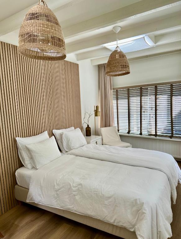 a bedroom with a large white bed with two pendant lights at Oranje Nassau aan Zee Studio in Zandvoort