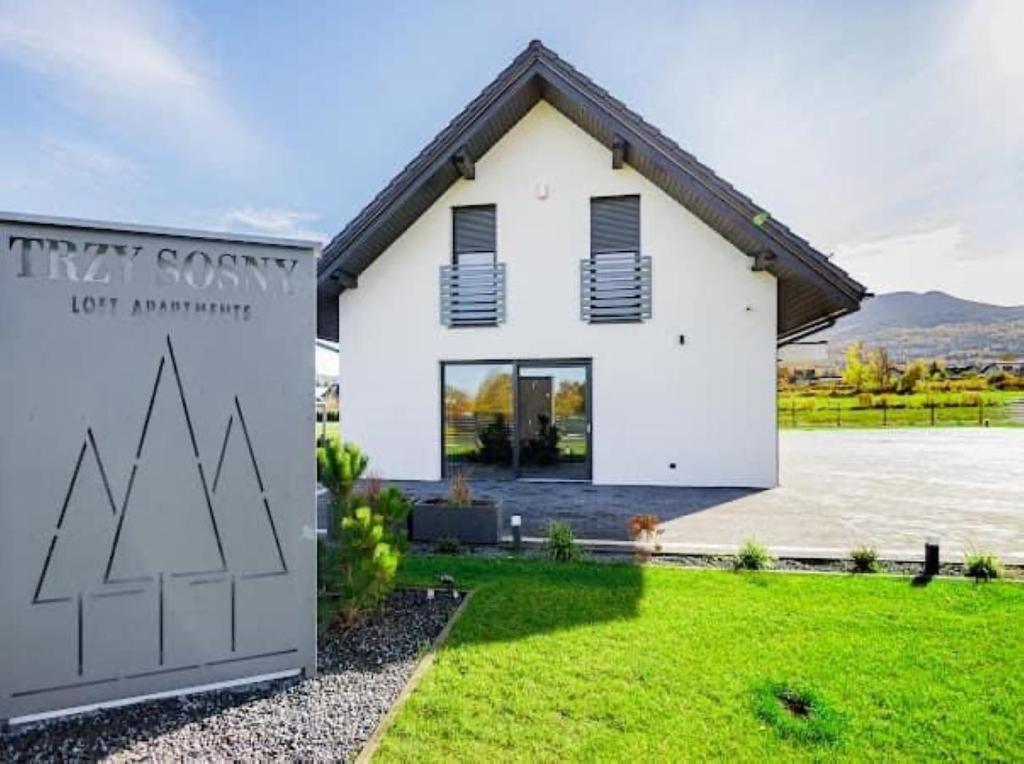 Uma casa branca com um cartaz à frente. em TRZY SOSNY LOFT APARTMENTS em Ściegny