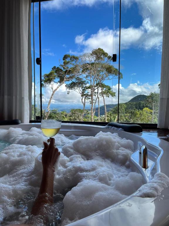 a person holding a drink in a bath tub with snow at Chales Labelle - 5 minutos do Centro Santa Teresa - 3 km in Santa Teresa