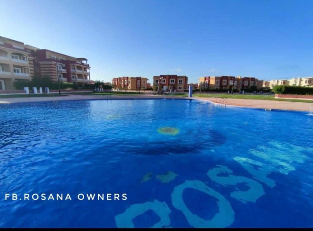 ein großer Pool mit blauem Wasser mit Gebäuden im Hintergrund in der Unterkunft Chalet Rosana Resort الساحل الشمالى in Dawwār al Ḩajj Aḩmad
